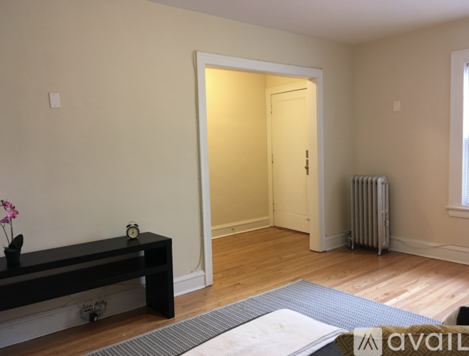 A room with a wooden floor, a bench, a radiator, and a door leading to another room.