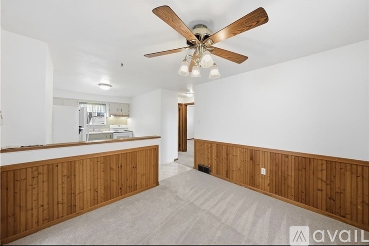 A spacious room with a ceiling fan and wooden paneling on the walls.