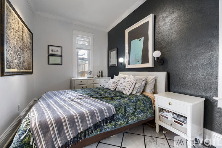 A bedroom with a bed, nightstand, and a painting on the wall.