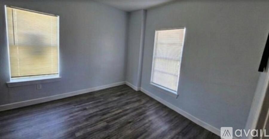 A room with wooden flooring and two windows.