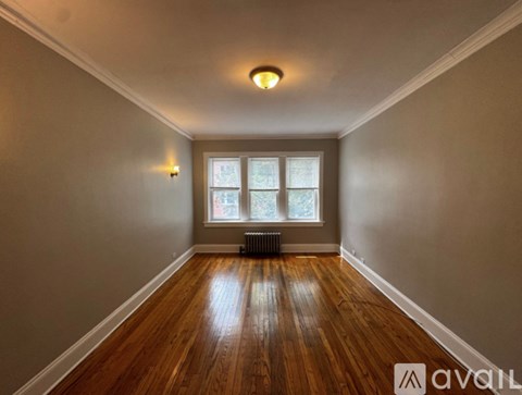 A room with wooden floors and a window with a radiator beneath it.