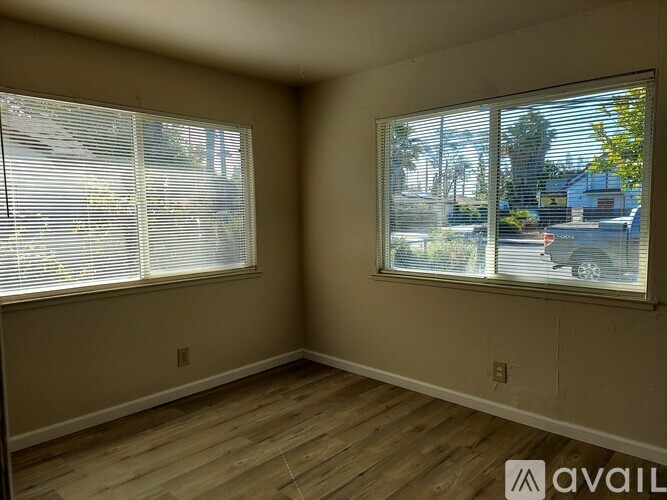 A room with wooden floors and two windows with blinds.