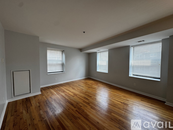 A spacious room with wooden floors and two windows.
