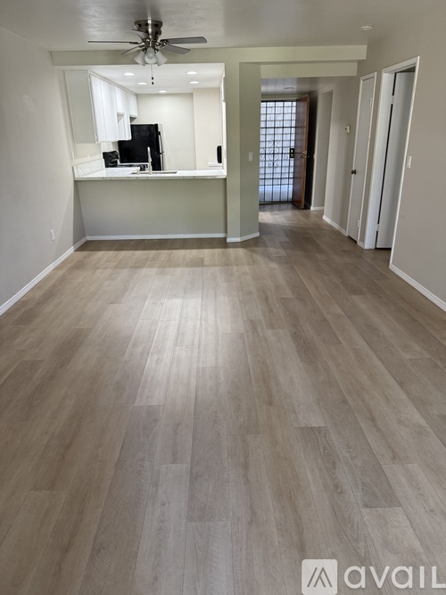 A spacious room with light wood flooring and a ceiling fan.