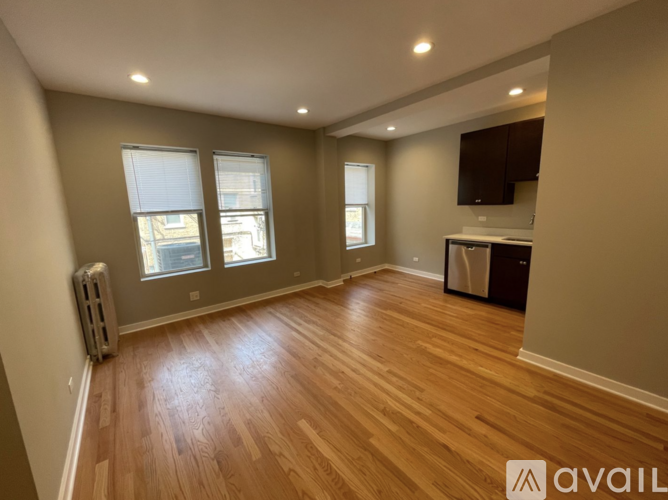 A spacious room with wooden flooring and a window with blinds.