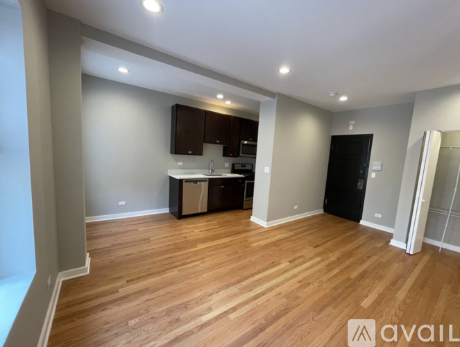 A spacious room with wooden flooring and a kitchenette.
