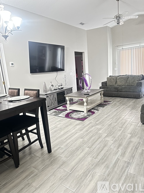 A living room with a grey couch, a wooden table, and a flat screen TV mounted on the wall.