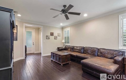 A living room with a brown leather couch and a ceiling fan.