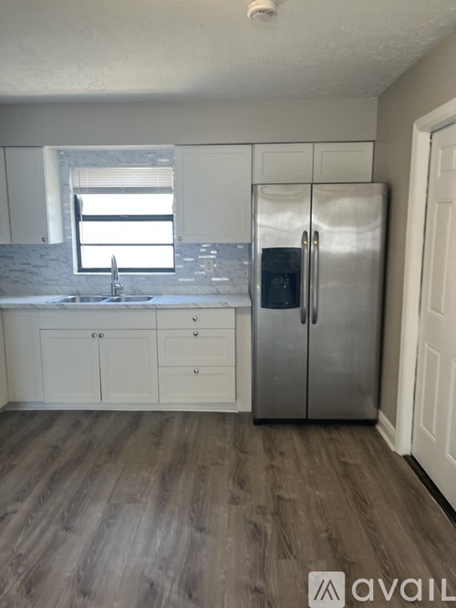 A kitchen with a stainless steel refrigerator and wooden flooring.