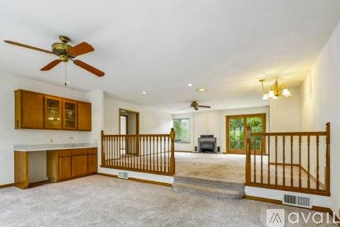 A spacious living room with a ceiling fan and a staircase leading to another room.