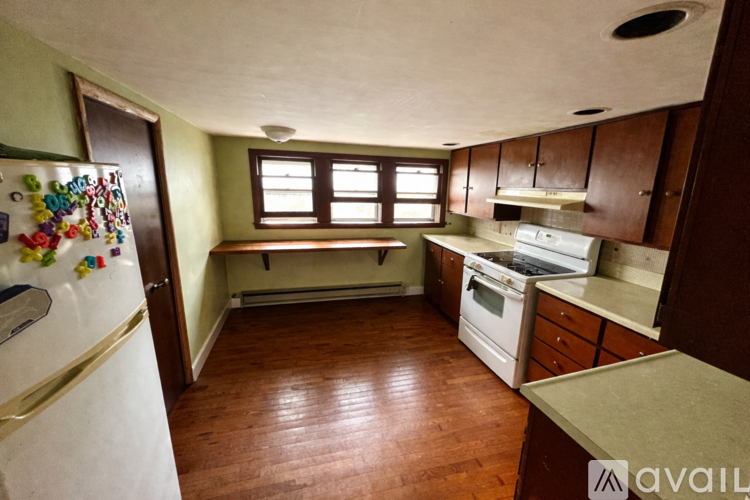 A kitchen with a refrigerator covered in magnets, a window with a view of a tree, and wooden floors.