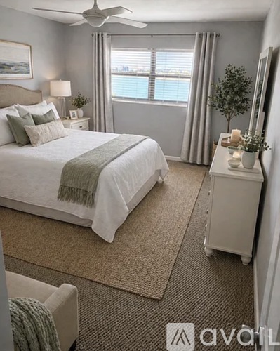 A bedroom with a large bed, a nightstand, and a window with a view of the water.