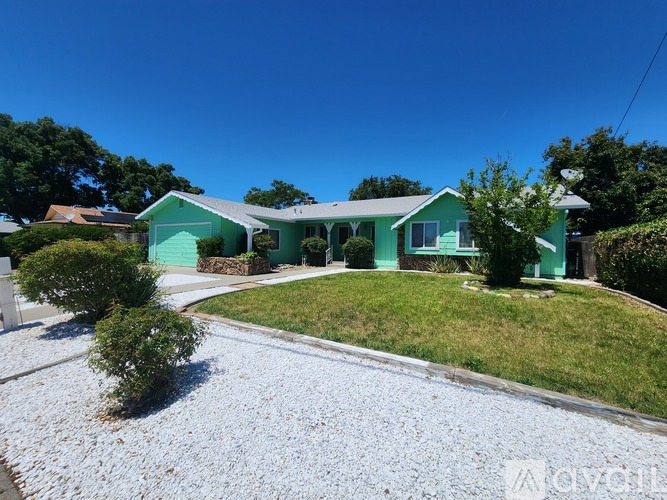 A green house with a gravel driveway in front.