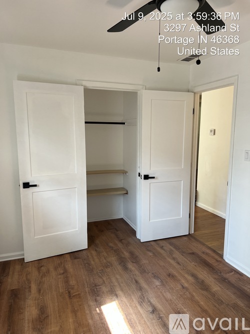 A room with a wooden floor and white walls, featuring two open doors.