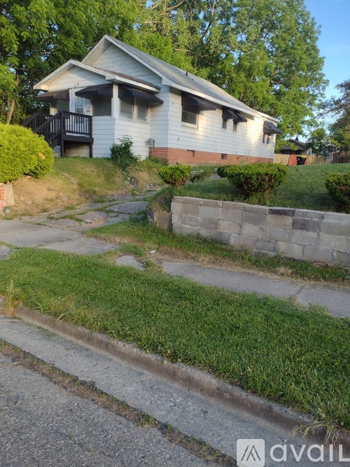 A house with a white siding and a grey roof is surrounded by a grassy area and a stone wall.