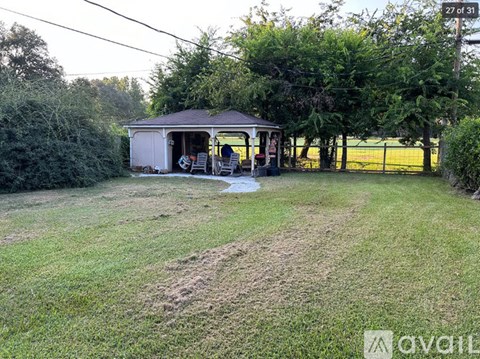 A gazebo is situated in a grassy area with trees and a fence in the background.