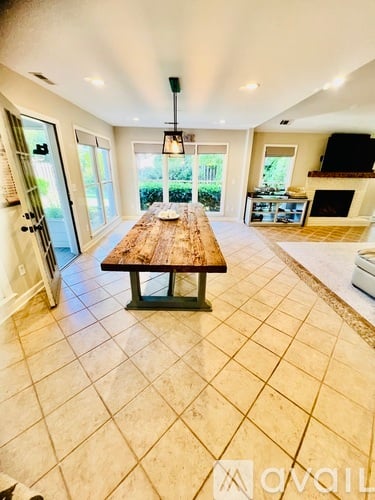 A large wooden table is in the middle of a spacious room with tile flooring.