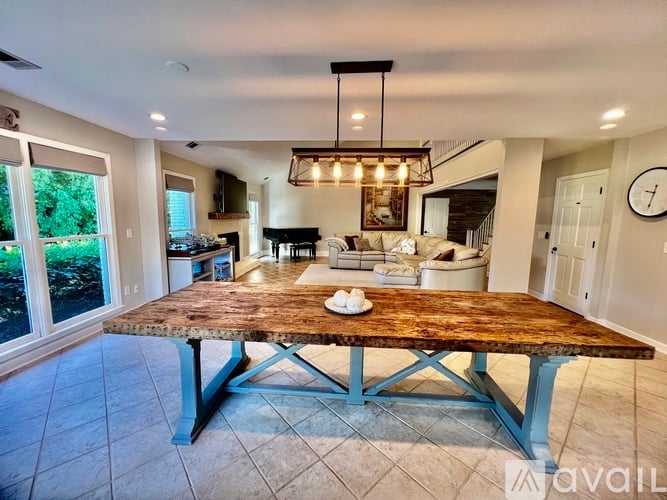 A large wooden table with a metal base is in the middle of a spacious room with a kitchen in the background.