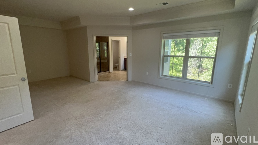A spacious room with a carpeted floor and a window overlooking trees.