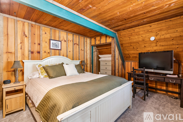 A bedroom with a bed, nightstand, and a television in a wooden cabin.