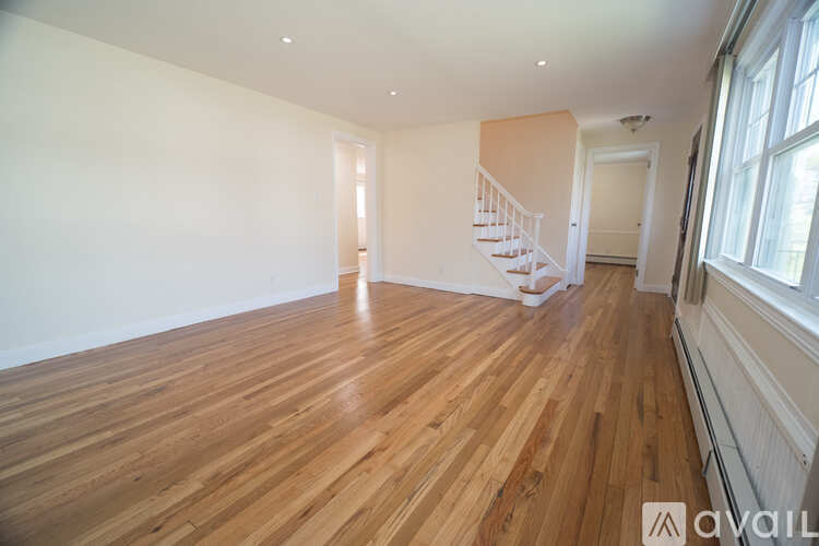 A room with wooden flooring and a staircase in the background.