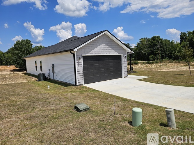 A white house with a grey roof and a garage door is surrounded by a grassy area.