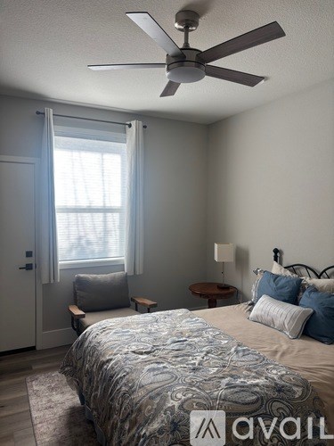 A bedroom with a bed, a fan, and a window with curtains.