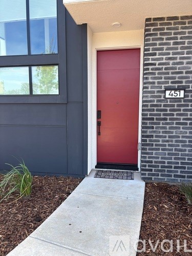 A red door with a black handle is on the side of a building with a brick wall.