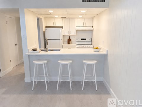 A kitchen with white cabinets and appliances, a bar area with stools, and a light wood floor.