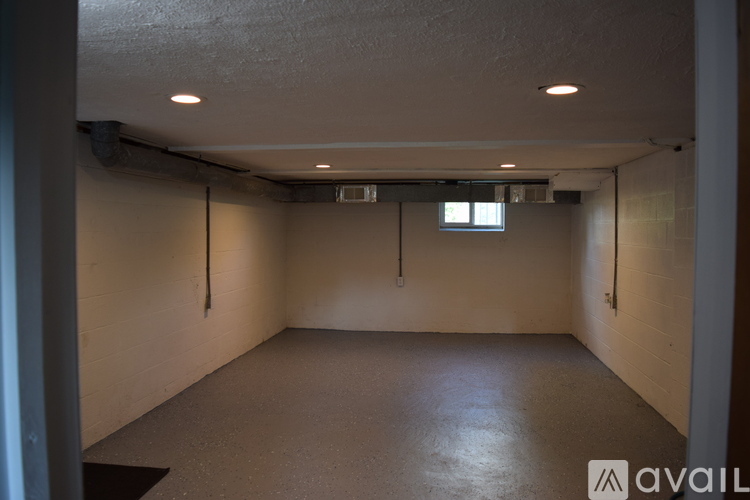 A spacious empty room with a window and fluorescent lights on the ceiling.