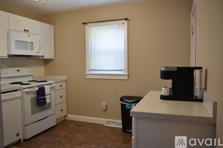 A kitchen with a white stove and microwave, a window with blinds, and a black coffee maker on the counter.