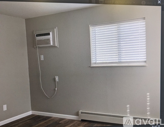 A room with a window covered by white blinds and a wall-mounted air conditioner unit.