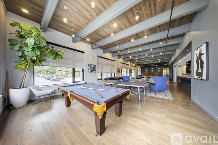 A pool table is in the middle of a room with a blue chair and a plant.