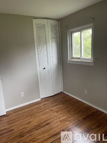 A room with a white door and a window with a view of trees outside.