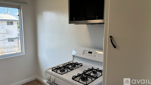 A white gas stove in a kitchen with a window and a microwave above it.