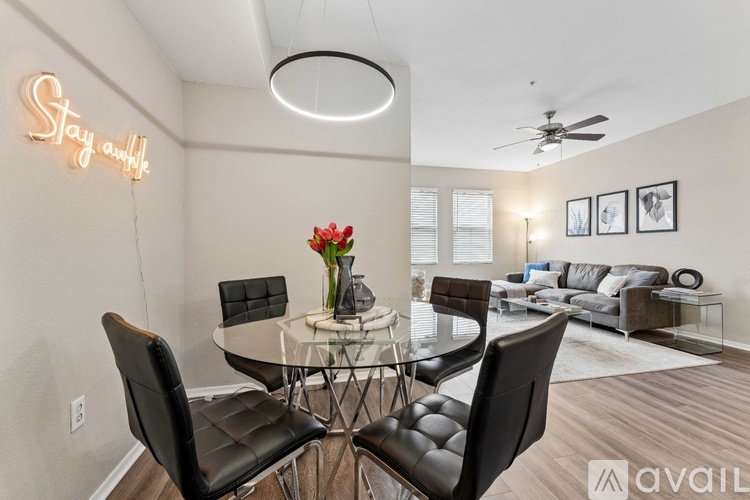 A modern dining room with a glass table and chairs, a ceiling fan, and a neon sign that says "Stay Awhile".