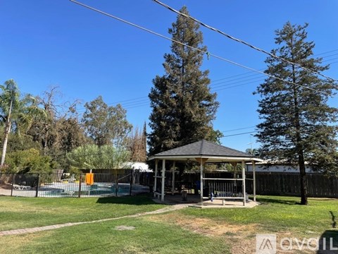 A gazebo is situated in a grassy area with a pool and trees in the background.