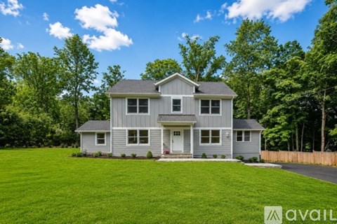 A house with a grey exterior is surrounded by a green lawn and trees.