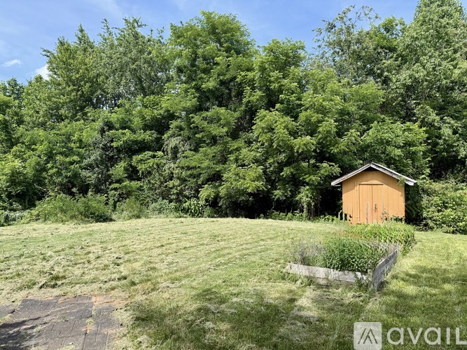 A small brown shed sits in a grassy field with trees in the background.