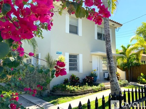 A white house with a black fence and pink flowers in front.