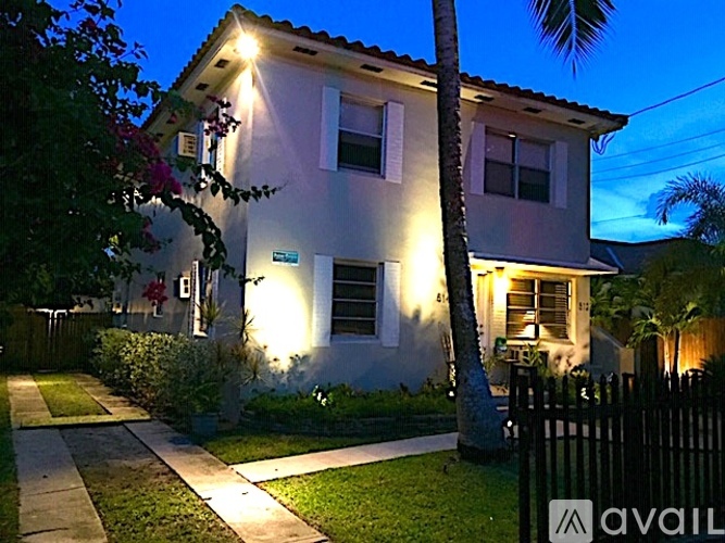 A house with a lit up front porch and a palm tree in front.