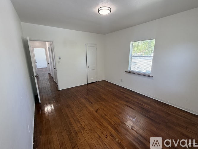 A room with wooden flooring and a window with a view of trees outside.