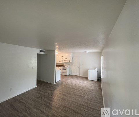 A spacious room with wood flooring and a kitchen area in the background.