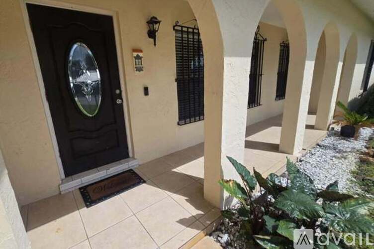 A black door with a round window is on the left side of a white building with arches.