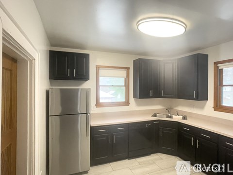 A kitchen with black cabinets and a stainless steel refrigerator.