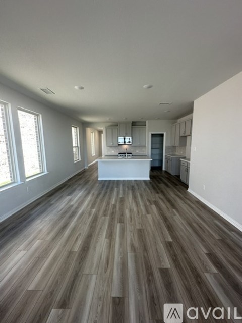 A spacious room with wooden flooring and a kitchen area in the background.