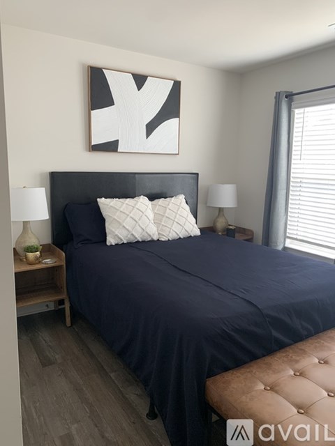 A bedroom with a dark blue bedspread and a white and black abstract painting above the bed.