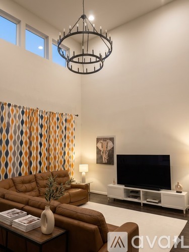 A living room with a brown leather couch, a white coffee table, a television, and a chandelier.