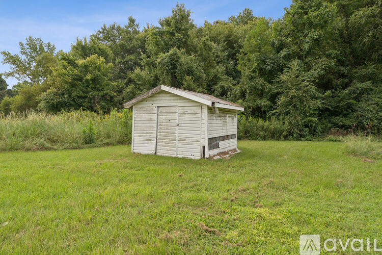 A shed sits in a grassy field with trees in the background.
