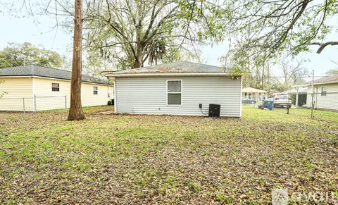 A small house with a grey roof is surrounded by a grassy area with fallen leaves.
